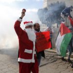 A Palestinian protester dressed in a Santa Claus costume rings a bell in front of tear gas fired by Israeli troops during a demonstration against the settlements and demanding for free movement for the Palestinians during Christmas near a checkpoint in the West Bank city of Bethlehem December 23, 2014.