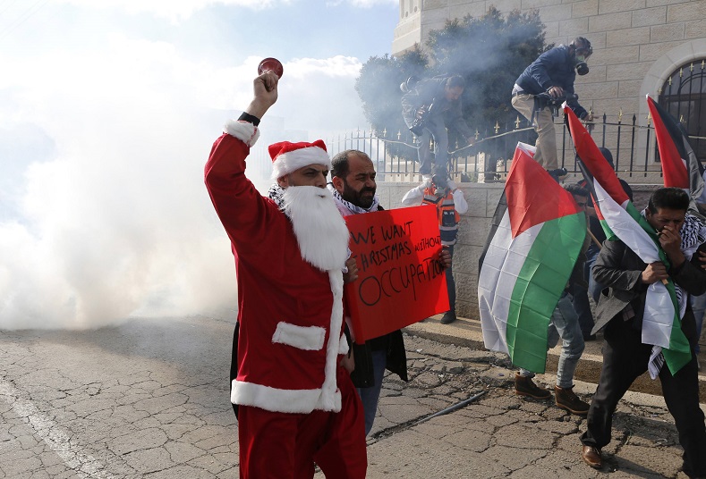A Palestinian protester dressed in a Santa Claus costume rings a bell in front of tear gas fired by Israeli troops during a demonstration against the settlements and demanding for free movement for the Palestinians during Christmas near a checkpoint in the West Bank city of Bethlehem December 23, 2014.