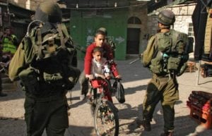 Palestinian children ride their bike past Israeli soldiers patrolling in the old city of Hebron in the West Bank. 