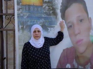 mom stands next to poster of her palestinian child who was killed by israel