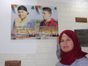 palestinian mom stands next to posters of children killed by israel in her village