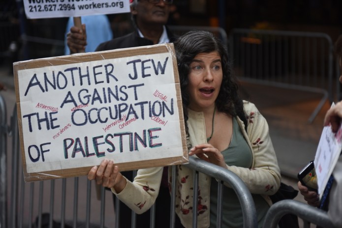 woman holds a sign that says, "another Jew against the occupation of Palestine"