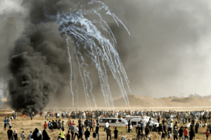 Amnesty International report on Israeli apartheid: Palestinian protesters run for cover after Israeli forces launched tear gas canisters during a demonstration along the border between the Gaza strip and Israel, east of Gaza city on June 22, 2018.