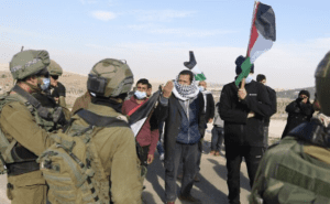 Palestinians protest Israeli policies and settler attacks in the south Hebron Hills as soldiers look on, January 2, 2021.