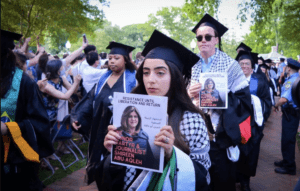 Nooran Alhamdan and her peers walking into the ceremony while holding posters of slain journalist Shireen Abu Akleh 