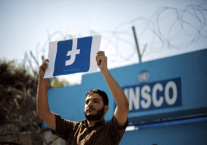 In protest of social media's failure to allow Palestinian voices their rights, a demonstrator holds an upside-down banner of the Facebook logo.