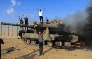 Palestinians celebrate as an Israeli military vehicle burns after it was hit by Palestinian gunmen who infiltrated areas of southern Israel, at the Israeli side of Israel-Gaza border, on October 7, 2023