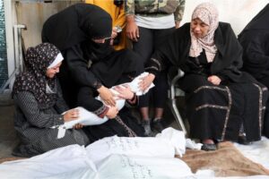 Women mourn as they hold the body of a Palestinian child killed in Israeli strikes on homes in Rafah, on December 7, 2023