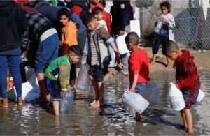 Children wade through puddles to fill bottles with water in Rafah