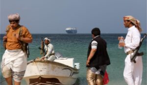 Armed men stand on the beach as the Galaxy Leader commercial ship, seized by Yemen's Houthis in December, is anchored off the coast of al-Salif, Yemen, December 5, 2023.