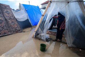 A Palestinian woman stands at the entrance of a tent flooded by heavy rain