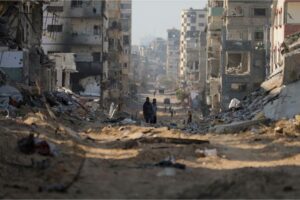 Palestinians walk between the remains of destroyed buildings following the Israeli bombardment on the main road of Gaza City on January 2, 2024