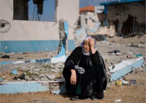 A woman rests next to a damaged building as Palestinians arrive in Rafah after they were evacuated from Nasser Hospital in Khan Younis, February 15, 2024