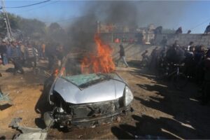 Palestinians watch a car burn after it was hit by an Israeli strike in Rafah