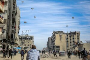 Palestinians run along a street as humanitarian aid is airdropped in Gaza City on Friday