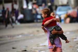 A Palestinian girl carries a toddler as people flee Rafah