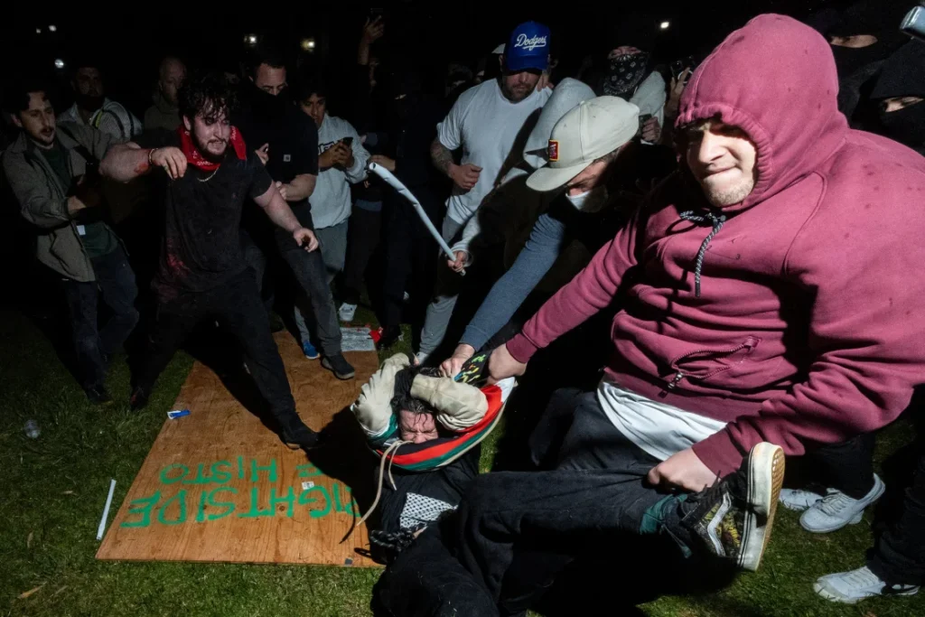 A pro-Palestinian demonstrator is beaten by counterprotesters attacking a pro-Palestinian encampment set up at UCLA's campus. The man in the maroon hoodie is among the attackers, which include Malachi Marlan-Librett (beige cap) to his right.