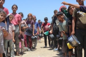 Palestinians, including children, line up for aid in Deir al-Balah amid Ongoing Israeli attacks on Gaza.