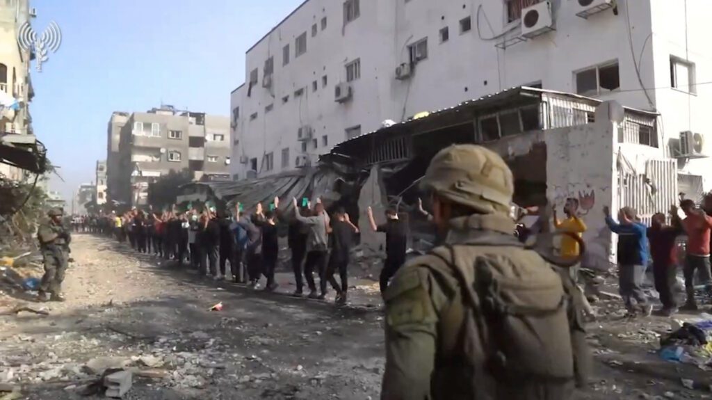 Israeli soldiers stand guard as men with raised hands are led out near Kamal Adwan Hospital in the northern Gaza Strip (Screen grab from an Israeli army video released on December 14, 2023 via Reuters)