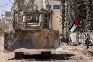 A Palestinian activist holding a national flag stands by as an Israeli army bulldozer moves during an ongoing raid on the Tulkarm camp for Palestinian refugees in the north of the occupied West Bank on September 12, 2024. [ZAIN JAAFAR/AFP via Getty Images]