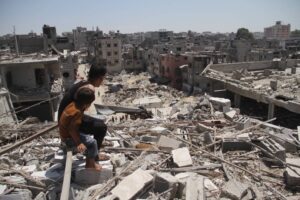 Two Palestinian children look at the displaced Palestinians who escaped from the Israeli army attacks and took shelter in the Jabalia Refugee Camp in the north of the Gaza Strip as they line up among the collapsed and heavily damaged buildings to receive food, distributed by charity organizations, Jabaliya, Gaza on August 26, 2024.