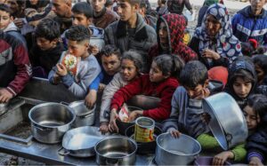 Palestinian people with empty bowls wait for food at a donation point in Rafah. 