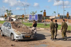 Israeli soldiers and a woman walk past a damaged vehicle in the aftermath of an Iranian missile attack on Israel, on October 2, 2024 in Tel Aviv.