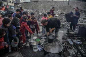 Palestinian children queue for receiving food as volunteers distribute food for Palestinian families ,displaced to Southern Gaza due to Israeli attacks, between rubbles of destroyed buildings in Rafah, Gaza.