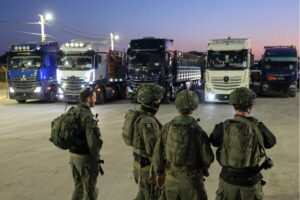 Israeli soldiers stand guard as trucks loaded with humanitarian aid delivered from Jordan wait to cross into Gaza, October 21, 2024. (Photo taken during a controlled tour by the Israeli military.) The Israeli military often allows gangs to loot aid trucks shortly after they enter Gaza.