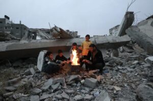 A Palestinian family tries to protect themselves from the cold weather by lighting a fire on the rubble of their house, in central Gaza, Dec. 26