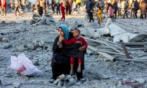 A woman sits with a child at the site of Israeli bombardment on a residential block in Jalaa Street in Gaza City, 14 January 2025.