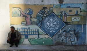 A man squats by a wall bearing a mural representing the UNRWA (United Nations Relief and Works Agency) at the aid agency's center at the Nuseirat camp in the central Gaza Strip on October 29, 2024, the day Israel's parliament approved a bill banning the agency from the devastated Gaza Strip.