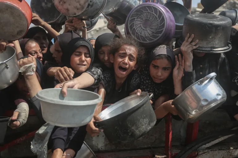 Starving Palestinians, including women and children holding pots, wait to receive food distributed by a charity organisation as Israel continues to block aid from reaching the Gaza Strip