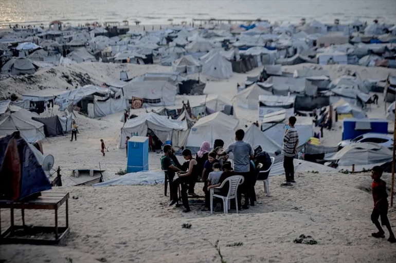 Palestinians sit around a table in a crowded tent camp by the beach in Gaza City, Monday, August 11, 2025