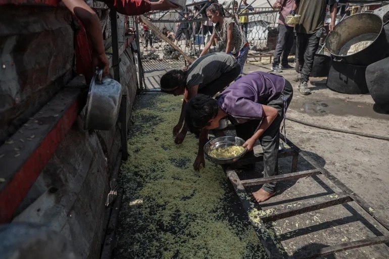 Children pick up the food scraps that have fallen on the floor during meal distribution by charity organizations