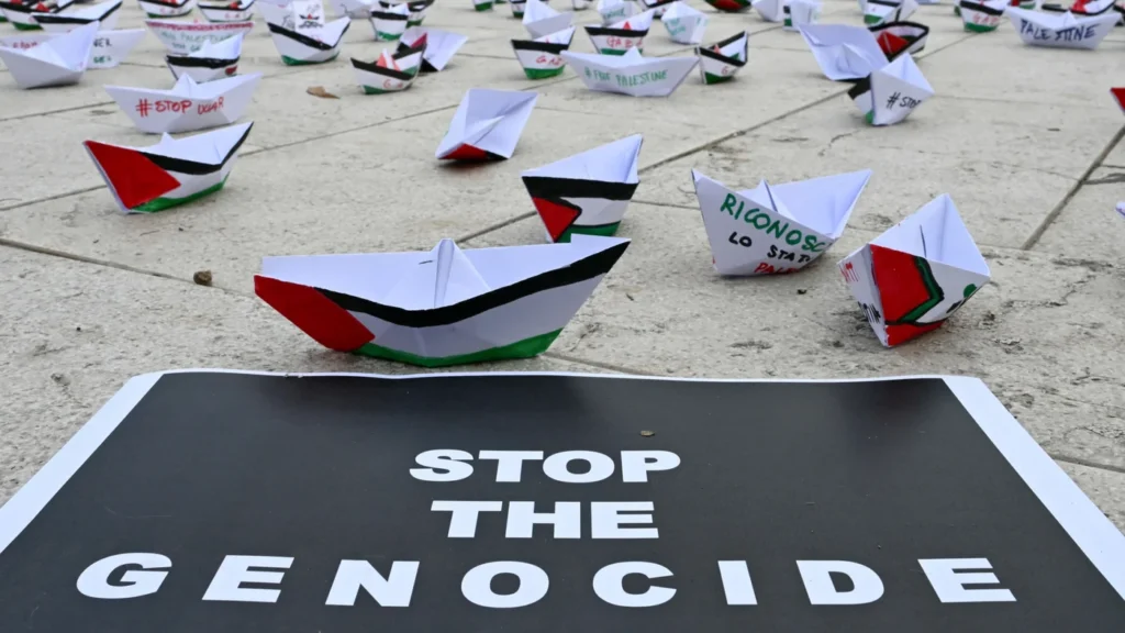 Paper boats and a 'Stop the genocide' poster at a Palestine solidarity protest during the Venice Film Festival on 30 August 2025
