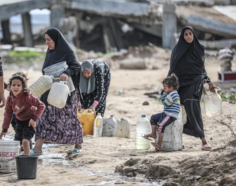 Palestinians living in the Bureij refugee camp in the central Gaza Strip, where infrastructure has been severely damaged and a water crisis has emerged as a result of Israeli attacks, carry water distributed by water tankers to their living areas in jerry cans, in Deir el-Balah, Gaza, on January 01, 2025