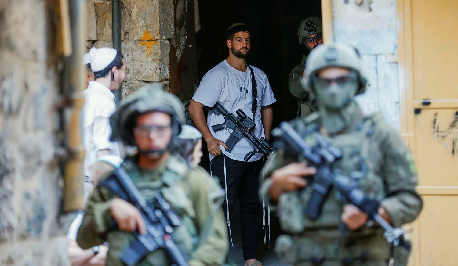An armed settler stands near Israeli troops during a weekly settlers' tour in Hebron, West Bank, August. Credit: Mussa Qawasma/Reuters