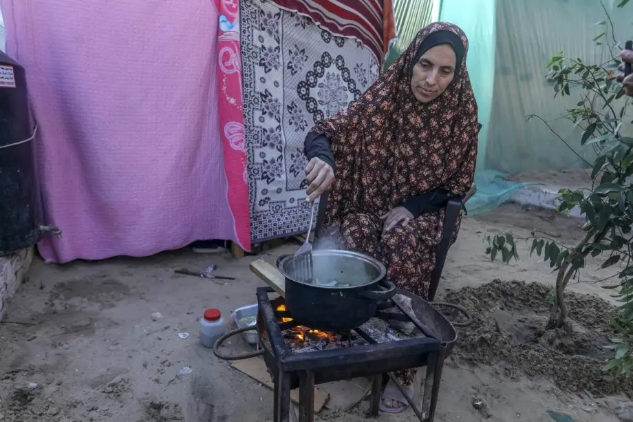 A woman cooks food as Palestinian families seek shelter in makeshift living spaces on the streets after leaving their houses for safety in Rafah, Gaza on January 09, 2023.