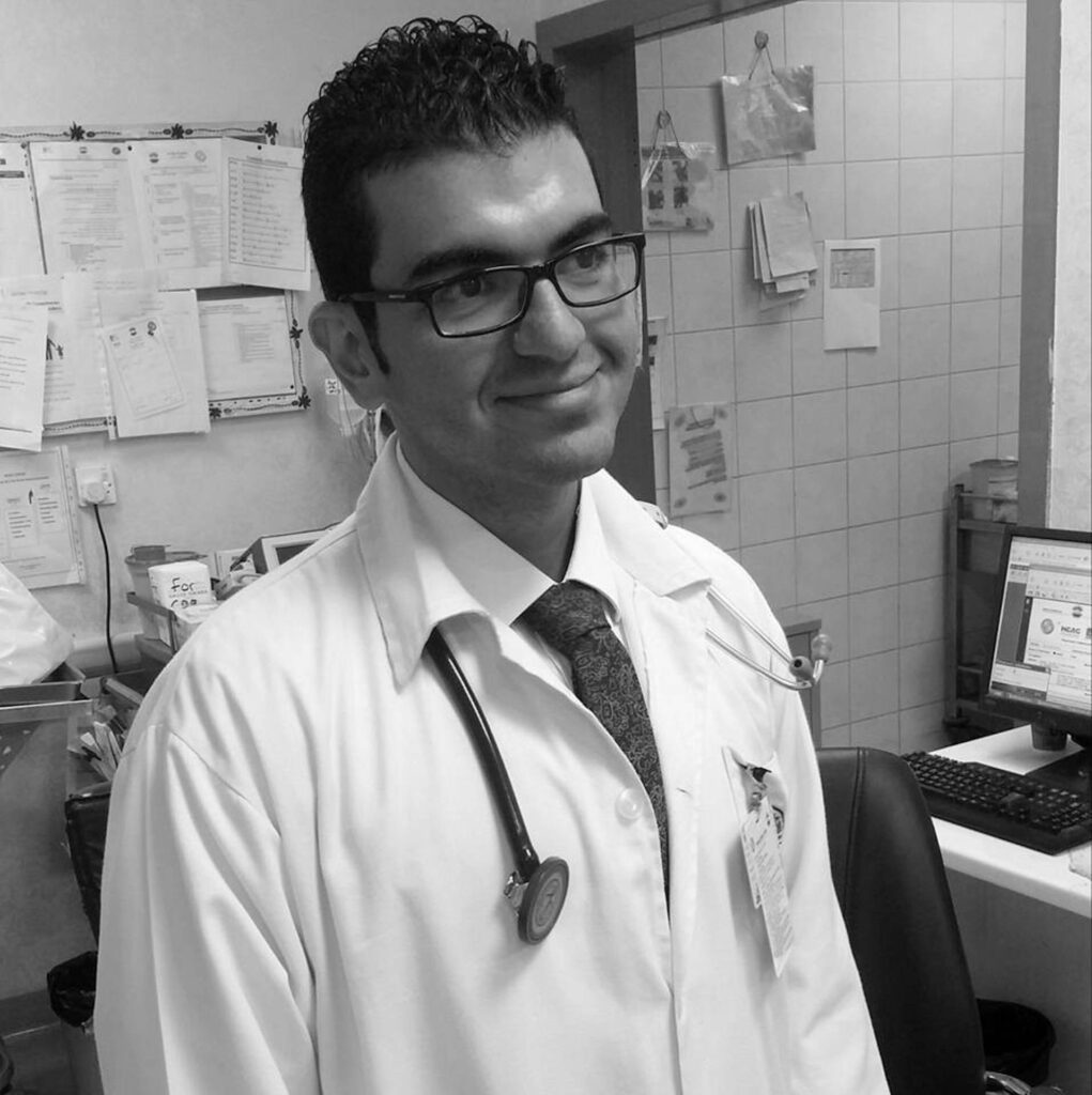 A doctor with glasses wearing a lab coat and stethoscope, in his office.
