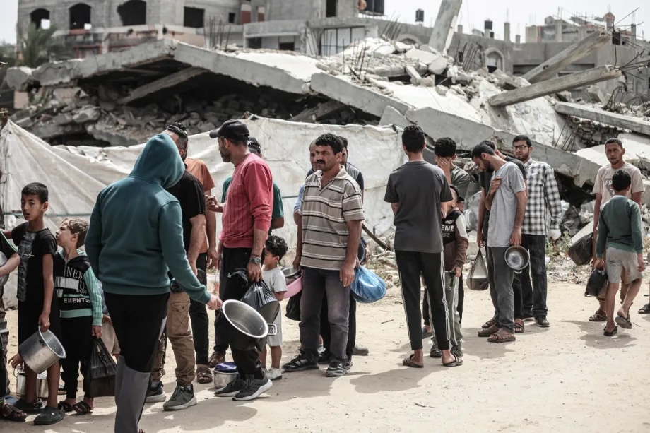 Displaced Palestinians, including many children, wait in long queues to receive hot meals distributed by a charitable organization at Bureijj Refugee Camp in Gaza City, Gaza, Palestine on May 18, 2026.