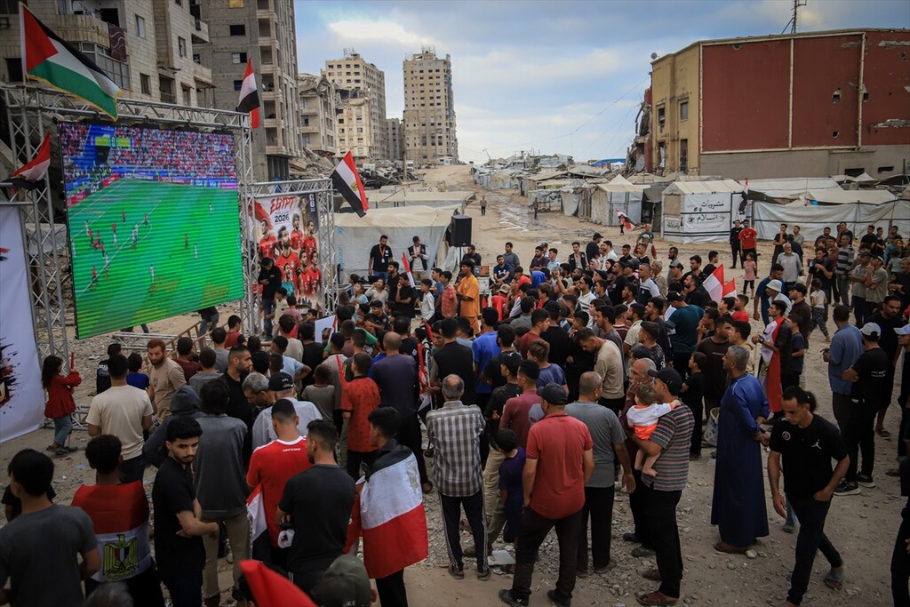 Palestinians holding flags gather to watch the 2026 FIFA World Cup First Stage Group G match between Egypt and Iran on a giant screen set up among the rubble of destroyed buildings despite Israel's ongoing attacks in Gaza City, Gaza, Palestine.