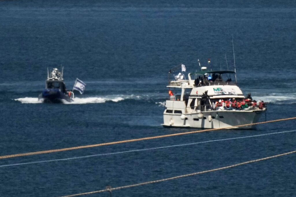 Activists in orange life jackets sit on a flotilla boat, intercepted while approaching the Gaza coast, as Israeli navy soldiers sail it into the port of Ashdod.