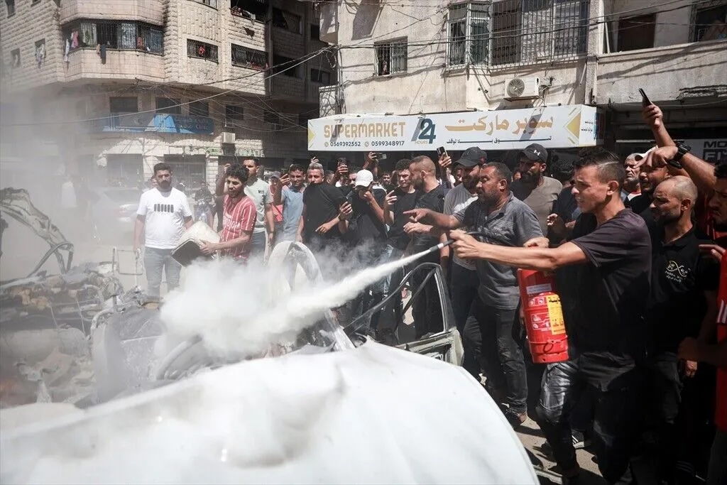Residents attempt to extinguish the fire that broke out in the vehicle following the attack after an Israeli drone strike targeted a civilian vehicle killing at least one Palestinian and injuring several others in western Gaza City, Gaza, Palestine